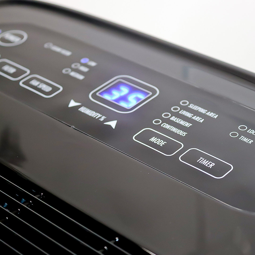 Black control panel with blue display and mode and timer buttons on dehumidifier