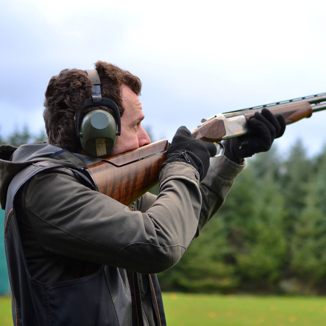Clay pigeon shooting experience: shooter aiming shotgun with ear protection and gloves