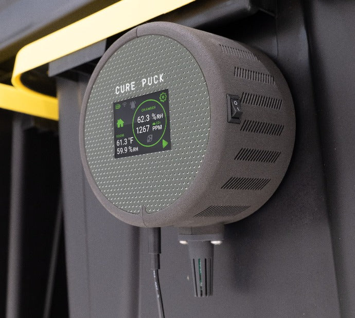 Grey round sensor puck with vents and green LCD status panel on a device mount